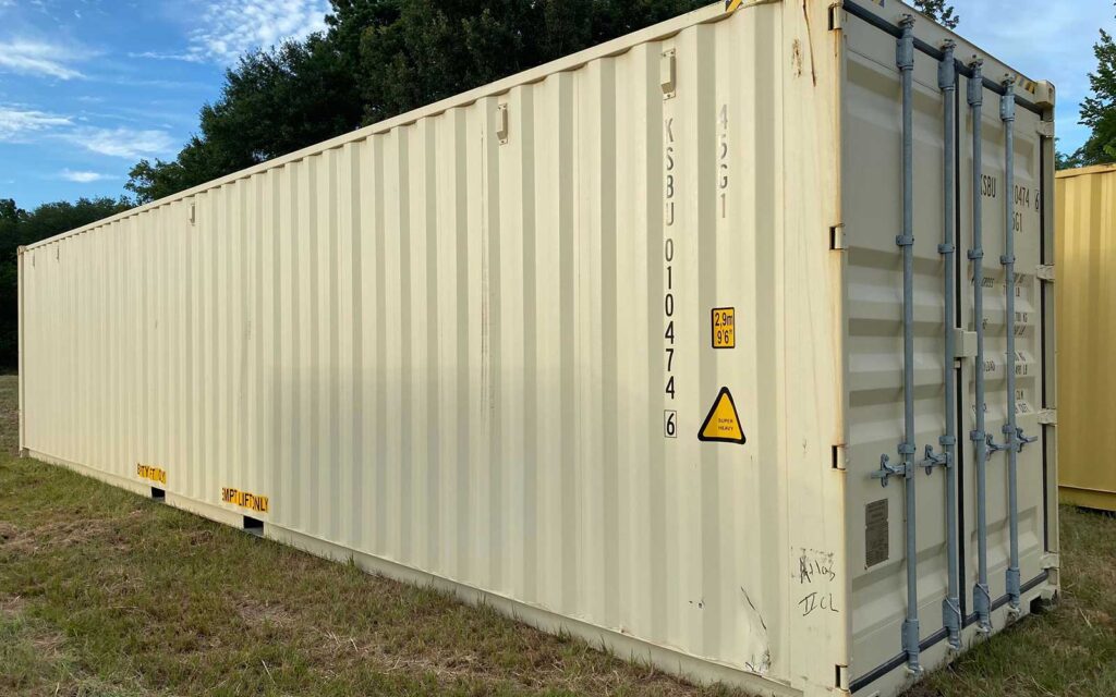 White shipping container on a grassy lot with trees and blue sky in the background, door area with vertical locking bars visible as a storage unit.
